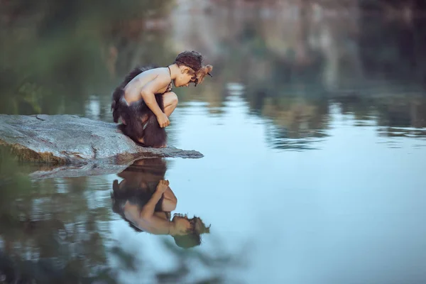 Caveman. Little boy sitting on the beach and looks at the water — Stock Image Caveman. Little boy sitting on the beach and looks at the water Stock Photo