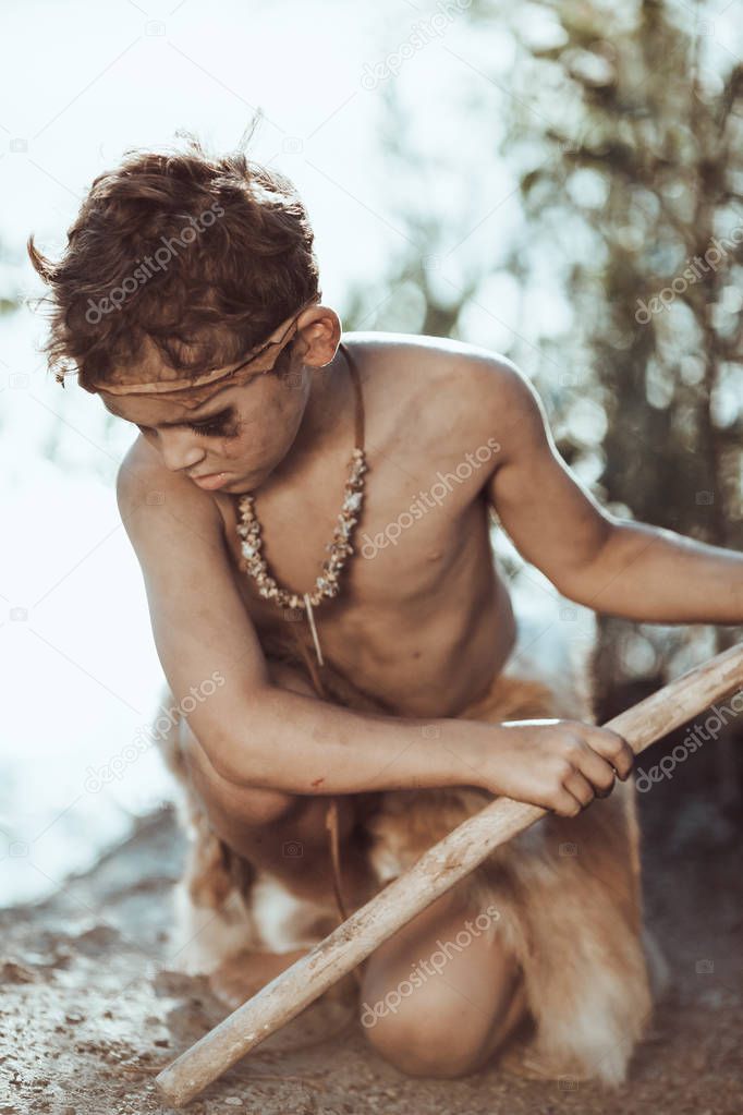 Cute caveman, manly boy with staff hunting outdoors. Ancient warrior