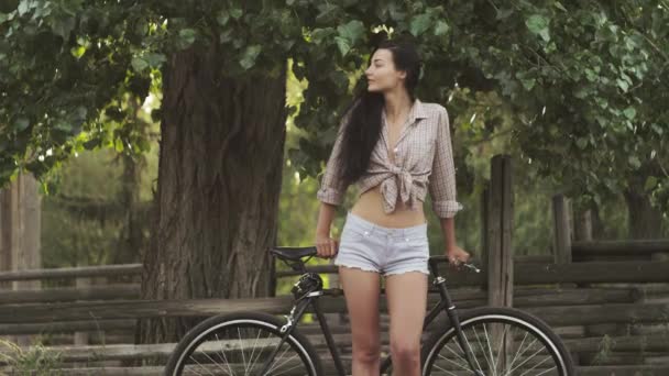 Mujer joven de pie con una bicicleta al aire libre — Vídeos de Stock