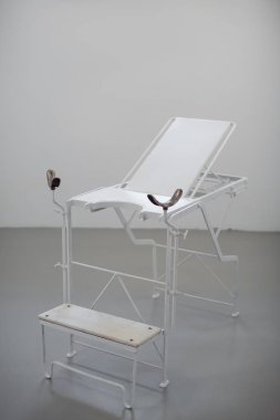 Old style chair for women diagnosis agaist white wall. Gynie exam table in museum.
