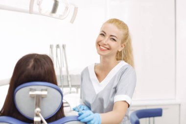 Dişçi ofisinde genç kadın ayakta ve kameraya bakıyor.