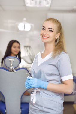 Dişçi ofisinde genç kadın ayakta ve kameraya bakıyor.