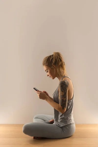 Mulher desportiva com smartphone sentado dentro de casa — Fotografia de Stock