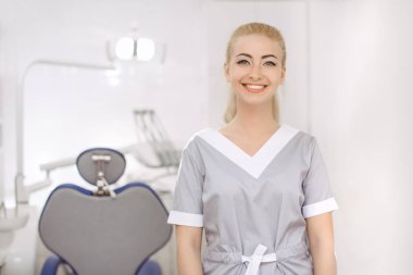 Dişçi ofisinde genç kadın ayakta ve kameraya bakıyor.