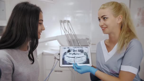 Dentista y paciente eligiendo el tratamiento en una consulta con equipo médico en el fondo — Vídeos de Stock