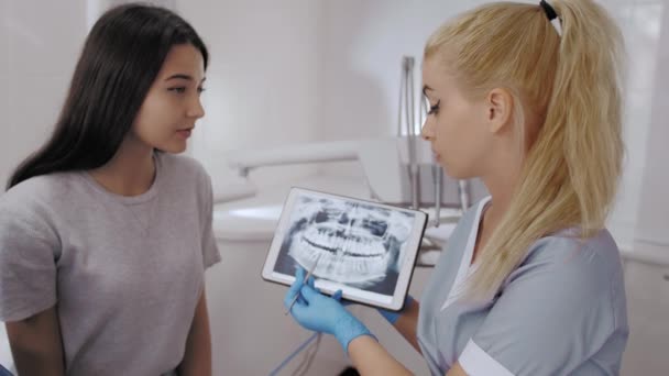 Dentista y paciente eligiendo el tratamiento en una consulta con equipo médico en el fondo — Vídeo de stock