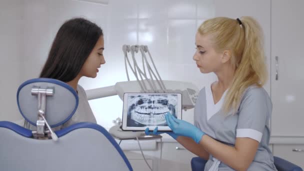 Dentista e paciente escolhendo tratamento em uma consulta com equipamentos médicos em segundo plano — Vídeo de Stock