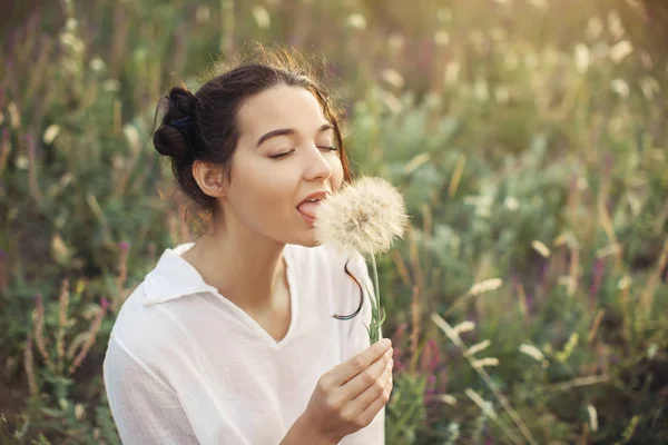 Mooie jonge vrouw met paardebloem in een tarweveld in de zomer zonsondergang. Schoonheid en zomer concept. Touch en feelengs. — Stockfoto