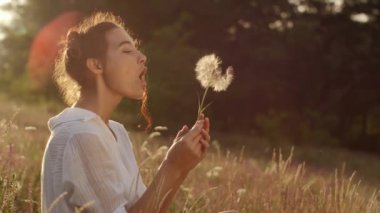 Güzel ve genç birbayan darbeler karahindiba yaz günbatımı buğday alanında. Güzellik ve yaz konsepti