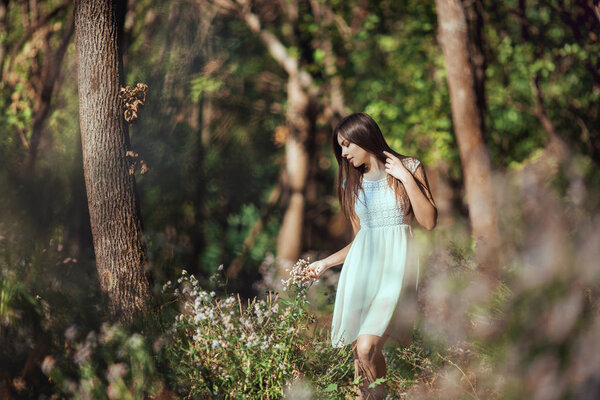 Beautiful young brunette woman walking and relaxing in the blossoming forest meadow on spring. Attractive girl enjoying spring sunny day on the nature