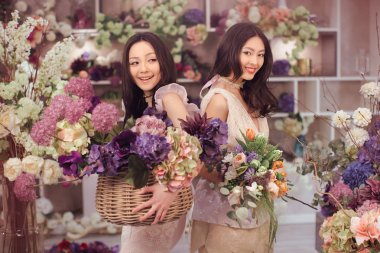Beautiful asian women florists happy working in flower store with a lot of spring flowers clipart
