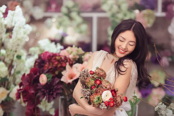 Hermosa mujer asiática florista en vestido blanco con ramo de flores en las manos en la tienda de flores — Foto de Stock