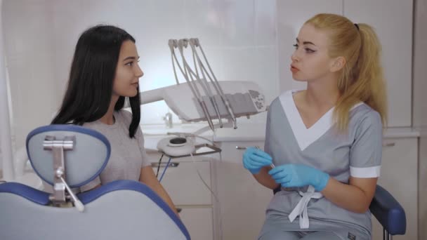Dentista y paciente eligiendo el tratamiento en una consulta con equipo médico en el fondo — Vídeos de Stock