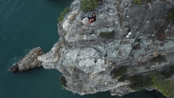 Вид с воздуха на молодую женщину на скале на берегу моря — стоковое видео