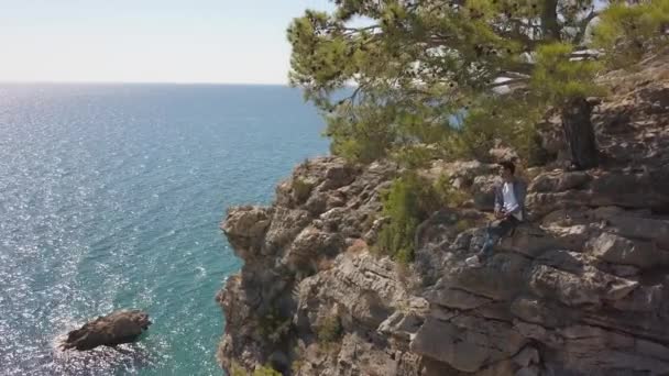 Vista aérea del joven viajero en el acantilado de roca contra el mar. — Vídeos de Stock