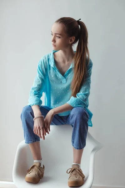 Vertrouwen stijlvolle stedelijke jonge vrouw op zoek weg terwijl zittend op stoel, op grijze achtergrond — Stockfoto