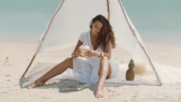 Vrouw drinkt kokosnoot sap terwijl ontspannen op het strand — Stockvideo