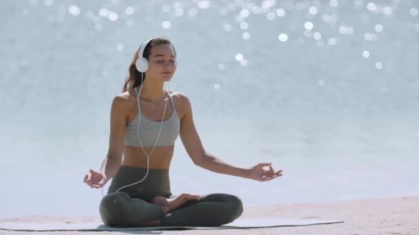 Woman in Yoga Meditation Pose με ακουστικά στην παραλία — Αρχείο Βίντεο