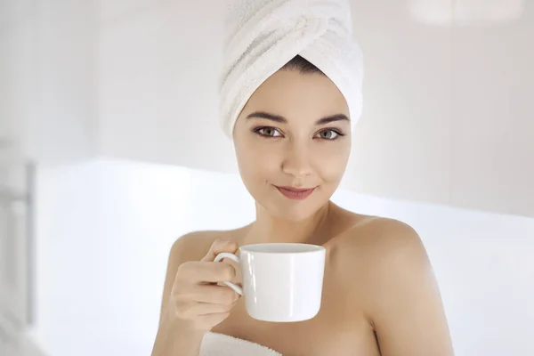 Mladá žena v ručníku těší kávu doma. — Stock fotografie