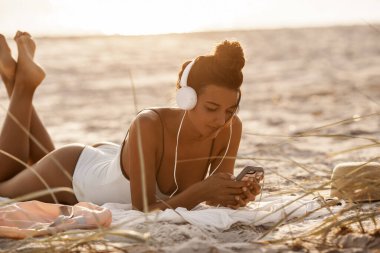 Bikini 'deki kumsalda akıllı telefonu ve kulaklığı olan kadın.