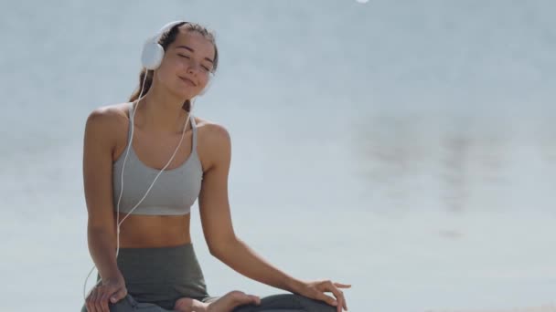 Kobieta w jodze Medytacja Pose ze słuchawkami na plaży — Wideo stockowe
