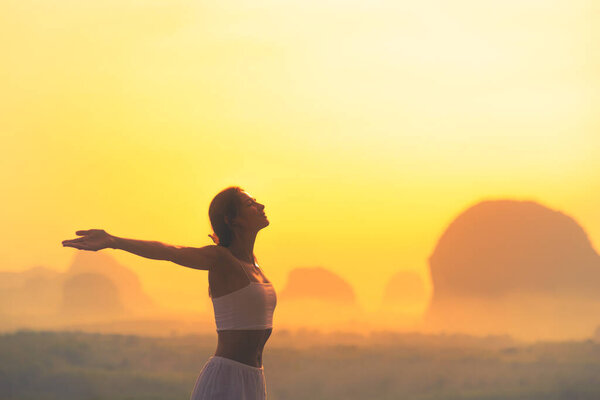 Silhouette of a woman in white outfit standing with arms wide open at sunrise in Krabi, Thailand. Inspiring and peaceful scene perfect for wellness, freedom, and lifestyle themes.