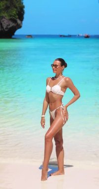 Beyaz kadın model, deniz kenarındaki beyaz bikinisiyle Maya Körfezi 'nde saçlarını zarafetle düzeltiyor. Yüksek kaliteli yaz yaşam tarzı, etkili ya da mayo içeriği için ideal.