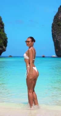 Beyaz bikinili kendine güvenen bir kadın Tayland 'ın Maya Körfezi' nde çarpıcı bir plajda kameraya gülümsüyor. Seksi, ışıl ışıl ve seyahat, yaşam tarzı ve moda tanıtımları için mükemmel.. 