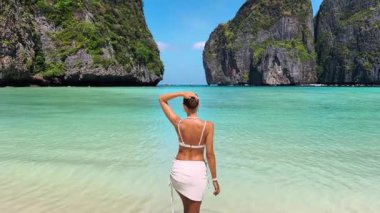 Maya Körfezi, Krabi, Tayland 'ın kumlu sahillerinde poz veren beyaz elbiseli genç bir kadın. Turkuaz su, egzotik uçurumlar ve yüksek kaliteli lüks seyahat yaşam tarzıyla mükemmel bir tropikal tatil sahnesi.