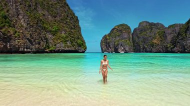 Beyaz bikinili manken turkuaz sudan çıkıp Tayland 'ın Maya Körfezi sahiline gidiyor. Seyahat, yaz, moda ve nüfuz kampanyaları için mükemmel. Yüksek kaliteli tropikal yaşam tarzı görüntüleri.