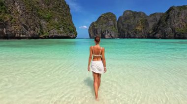 Maya Körfezi, Krabi, Tayland 'da beyaz elbiseli zarif bir kadın turkuaz suya doğru yürüyor. Sahne yavaş çekim seyahat konsepti egzotik tatil tanıtımı ve yüksek kaliteli yaşam tarzı için mükemmel