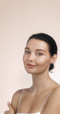 Beyaz tenli güzel bir kadın ve yumuşak bir gülümsemesi var. Güzellik reklamları, cilt ürünleri promosyonları ve sağlık markası görselleri için stüdyoda poz veriyor..