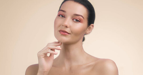 Крупный план молодой женщины с коралловыми тенями для век и светящейся натуральной кожей на мягком бежевом фоне. Идеально подходит для редакционного содержания красоты, рекламы по уходу за кожей и современных рекламных кампаний косметики.