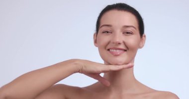 Çekici beyaz kadın gülümserken nazikçe çenesine dokunuyor, doğal cilt bakımını ve sağlığını destekliyor. Kozmetik, kaplıca ya da dermatoloji reklamları için kavramsal güzellik klipsi. 