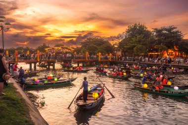 Vietnam, Hoi An 'daki Thu Bon nehrinin üzerinde canlı bir günbatımı. Turistler kalabalık bir köprünün yanında renkli fenerlerle geleneksel teknelerle gezmekten hoşlanırlar. Seyahat reklamı için yüksek kaliteli kavramsal fotoğraf.