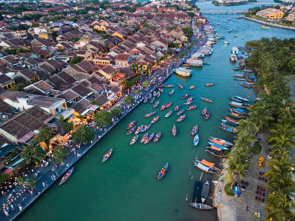 Hoi An, Vietnam 'da renkli tekneler nehirde süzülüyor. Fenerler tarihi sokakları aydınlatırken. Kültürel turizm ve Güneydoğu Asya 'daki canlı şehir yaşamının sergilendiği çarpıcı bir insansız hava aracı fotoğrafı.