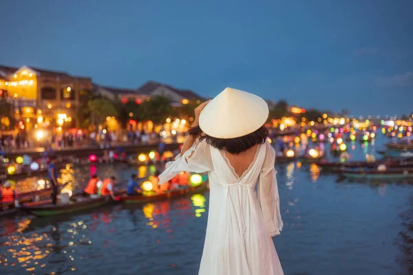 Beyaz elbiseli ve şapkasız zarif Asyalı kadının arka planında Hoi An 'ın parlayan fener teknelerine hayranlık duyuyordu. Seyahat tanıtımı, kültürel reklamlar ve hedef kampanyalar için ideal..