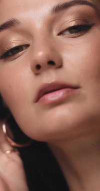 Kendine güvenen, altın makyajlı, yüzüne ve saçlarına hafifçe dokunan bir kadının yavaş çekim videosu. Güzellik reklamları, lüks cilt bakımı, kozmetik promosyonları ve editoryal moda içeriği için ideal.