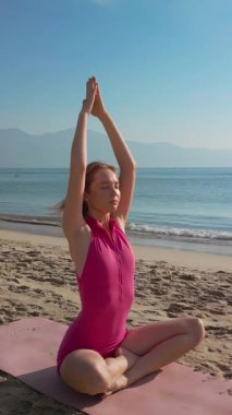 Plajda pembe mayoyla yoga yapan beyaz bir kadının sakin bir sahnesi. Sağlık, seyahat, yaşam tarzı ve meditasyon kavramları veya tanıtım videoları için ideal.