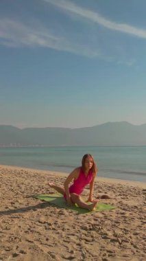 Pembe spor kıyafetli genç bir kadın, kumlu sahilde, okyanus manzaralı bir şekilde yoga yapıyor. Yüksek kalite sağlık ve yaşam tarzı konsepti, fitness reklamları, meditasyon tanıtımları ve sağlık kampanyaları için mükemmel..