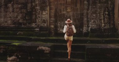 Sırt çantalı bir kadın Kamboçya 'daki antik tapınağa doğru yürüyor, kamera yukarı eğildiğinde taş kapıya dokunuyor ve çerçeveliyor. Tarih, macera, yaşam tarzı, kültür turizmi, tanıtım ve seyahat kavramı.