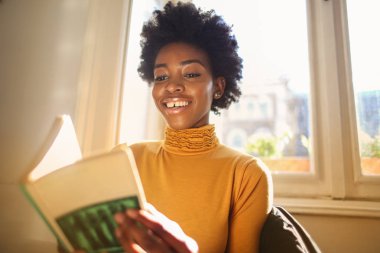 Bir kitap okuma ve gülümseyen genç Afro kadın.