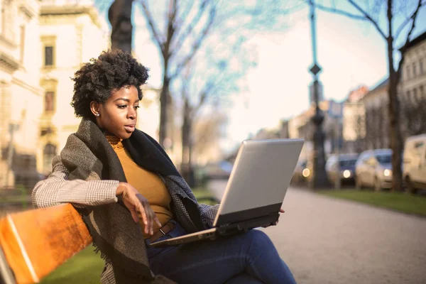 年轻漂亮的非洲妇女坐在长椅上 她的笔记本电脑和工作 — 图库照片