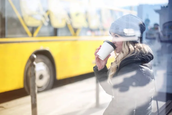 冬の市のバス停でコーヒーを飲みながら金髪の女性 — ストック写真