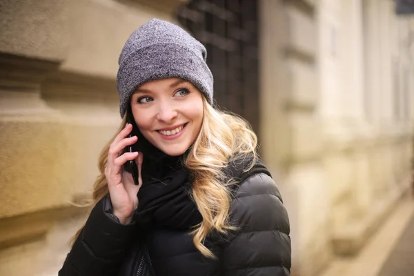 年轻美丽的金发女郎走在街上 谈论在一个智能手机在冬季 — 图库照片