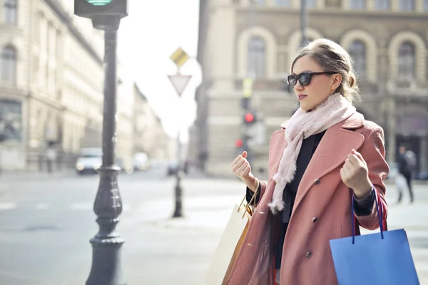 年轻的金发女郎走在城市与购物袋和太阳镜 — 图库照片