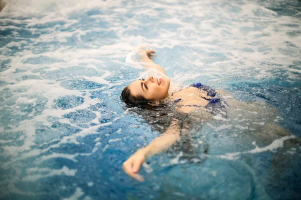 Rahatlatıcı ve havuzda yüzen güzel genç kadın.