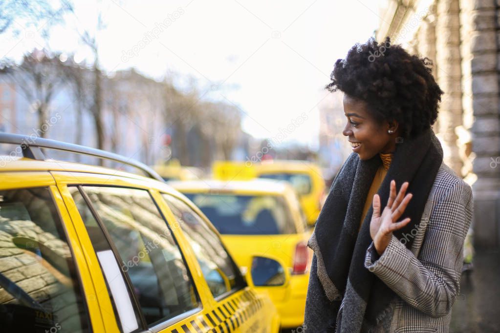 Young beautiful Afro woman taking a taxi in the city.