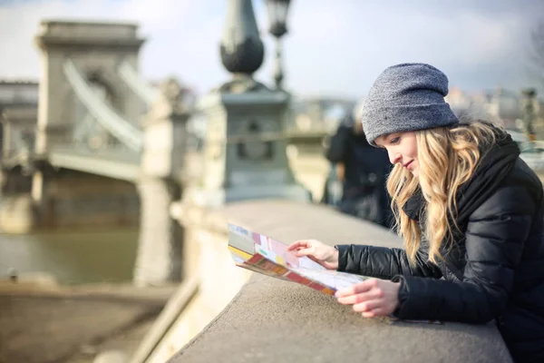 美丽的年轻金发女郎在冬季衣服检查她的地图旁边的桥梁 — 图库照片