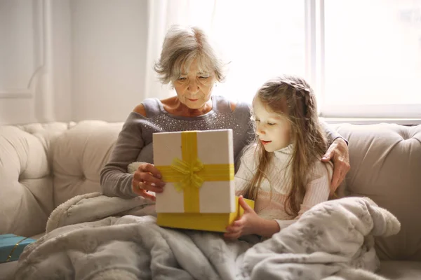 祖母と孫娘がソファで一緒にプレゼントを開いています — ストック写真